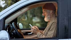 Happy older man traveler sitting in camper van using mobile in camping.