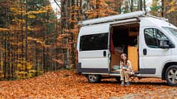 Woman eating lunch while sitting near the camper van in forest in autumn