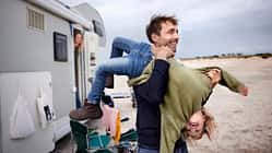 Playful father carrying girl at camper van on the beach