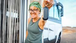 Happy new buyer owner of camper van motorhome show at the camera her keys with happiness. New house and vehicle for vacation concept scene. Travel vanlife lifestyle. Adventure. Nomadic people female