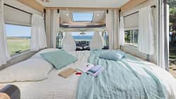 Gemachtes Hubbett im Mooveo TEI-70 DH (2027) mit Bettwäsche, Kissen und Buch, helle LED-Beleuchtung und Panorama-Dachfenster für natürliches Licht.