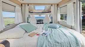 Gemachtes Hubbett im Mooveo TEI-70 DH (2027) mit Bettwäsche, Kissen und Buch, helle LED-Beleuchtung und Panorama-Dachfenster für natürliches Licht.