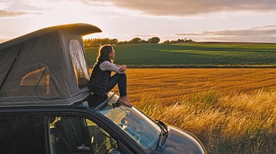Woman sitting on roof of campervan at sunset