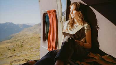 Woman reading book in camper van in mountains