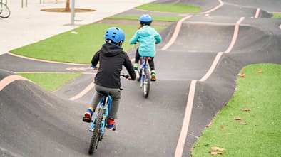 Kids riding a bike on a concrete pumptrack.