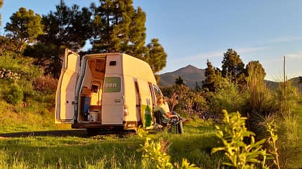 Elektro-Camper, Gras, Sträucher, Bäume, Berge, Mann, Klappstuhl, La Palma Elektro-Camper, Gras, Sträucher, Bäume, Berge, Mann, Klappstuhl, La Palma