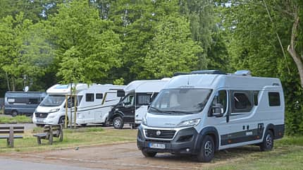 Mehrere Wohnmobile, darunter ein Pössl Trenta 640, stehen auf einem Stellplatz am Krandelbad in Wildeshausen, umgeben von Bäumen.