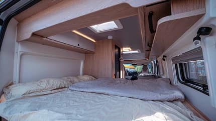Bett, Matratze, Dachstauschränke, Fenster, Decke Schlafplatz im Hobby ONTOUR VAN: Französisches Bett mit Kaltschaum-Matratze, Dachstauschränke und Fenster für natürliches Licht.