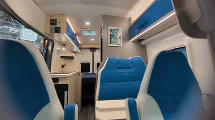 Durchschuss, blaue Polster, blaue Möbelfronten, Flugzeuglook Blick durch den Innenraum des Campingbusses mit blauen Polstern und blauen Möbelfronten im Flugzeuglook.