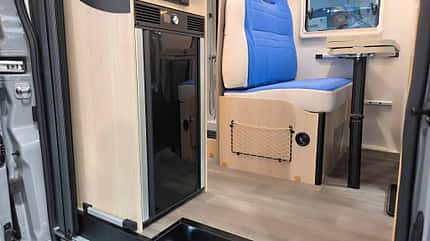 Kopfseitig eingebauter Kühlschrank, Aufbewahrungstasche an Sitzgruppe im Netz-Stil erinnert an Flugzeug Kopfseitig eingebauter Kühlschrank neben einer netzartigen Aufbewahrungstasche an der Sitzgruppe.