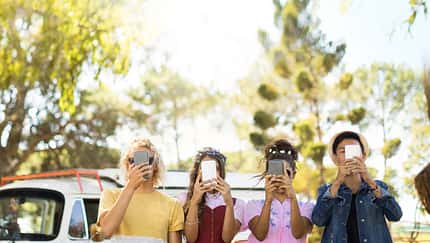 Vier junge Erwachsene stehen mit dem Smartphone vor dem Gesicht da