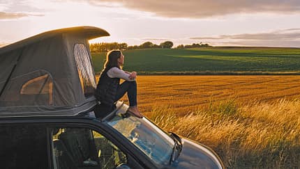 Woman sitting on roof of campervan at sunset