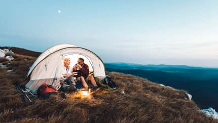 Senior couple camping in the mountains and eating a snack