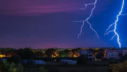 Two large and powerful lighting strikes crossing night blue sky
