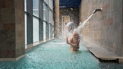 Side view of a man enjoying water massage in a pool under a waterfall jet in health spa