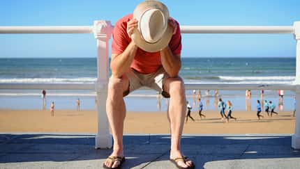 Symbolbild: Mann sitzt frustriert am Strand