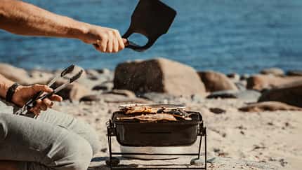 Fanning hot coals with a hand fan while grilling fish on the seaside