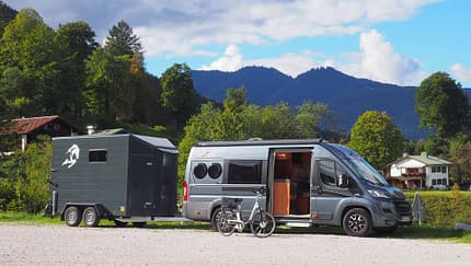 Gray camper van with a horse trailer in a parking lot