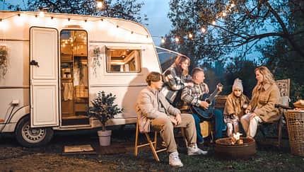Family trailer travel.Children,brother sister,mom dad playing guitar,singing song at fire.Evening picnic in nature.Holiday barbecue BBQ food.Vacation weekend dinner.Road lunch.Camper,house on wheels
