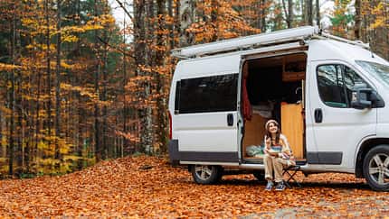 Woman eating lunch while sitting near the camper van in forest in autumn