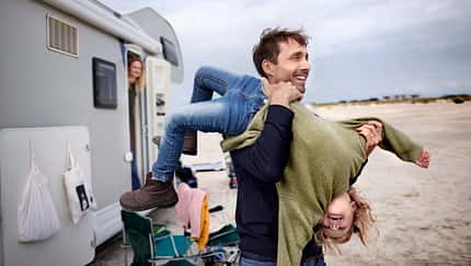 Playful father carrying girl at camper van on the beach