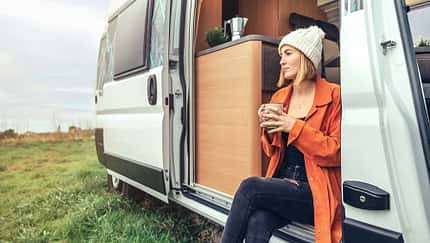 open door,pom pom hat Woman drinking coffee sitting at the door of a campervan