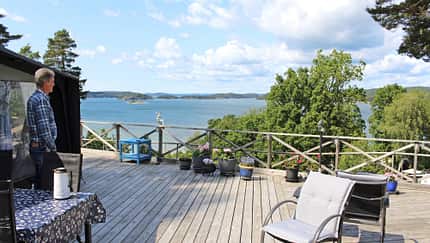 Schweden, Terrasse, Seeblick, Gartenmöbel, Blumentöpfe, Landschaft, Sommer, Holzdeck, Mann, Skandinavien Terrasse mit Blick auf einen See in Schweden, ein Mann steht am Rand, Gartenmöbel und Blumentöpfe sichtbar.