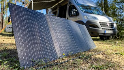 Solarpanel, Campingbus, Photovoltaik, Camping, Stromversorgung, Outdoor, Vanlife, Solarmodul, Energieversorgung, Wald Tragbares Solarpanel auf dem Boden vor einem Campingbus im Wald.