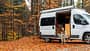 Woman eating lunch while sitting near the camper van in forest in autumn