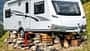 Wohnwagen, Camping, Alpen, Berge, Aufbocken, Reisemobil, Outdoor, Sommer, Campingplatz Wohnwagen aufgebockt auf Steinen und Holz in alpiner Berglandschaft, keine spezifische Modellbezeichnung im Dateinamen.