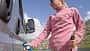 Woman plugging her camper van to recharge the battery, wind turbine in the background