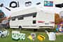 Ein Caravan wird von einem Auto gezogen. Drumherum ist Zubehör fürs Camping platziert.