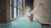 Side view of a man enjoying water massage in a pool under a waterfall jet in health spa