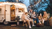 Family trailer travel.Children,brother sister,mom dad playing guitar,singing song at fire.Evening picnic in nature.Holiday barbecue BBQ food.Vacation weekend dinner.Road lunch.Camper,house on wheels