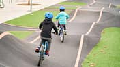 Kids riding a bike on a concrete pumptrack.